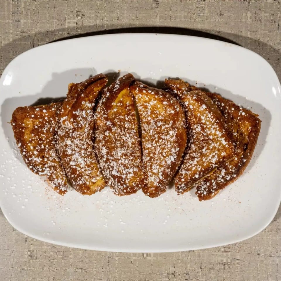 Golden brown French toast sticks, dusted with powdered sugar, arranged on a white rectangular plate.