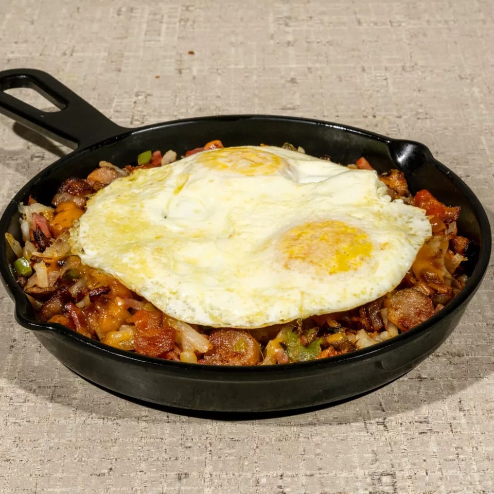 Breakfast skillet with fried eggs, sausage, potatoes, onions, and peppers in a cast iron pan.
