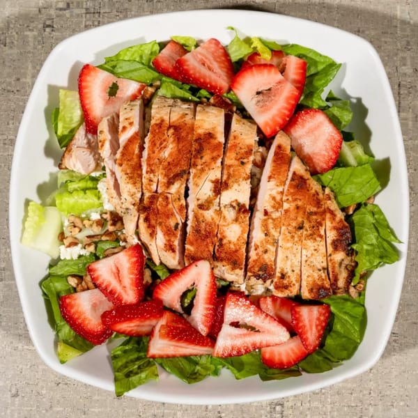 Overhead view of a grilled chicken and strawberry salad with lettuce, nuts, and feta cheese.
