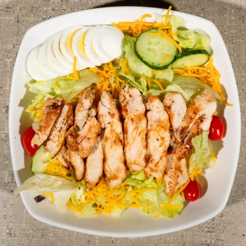 Grilled chicken salad with lettuce, shredded cheese, cucumber, cherry tomatoes, and sliced hard-boiled eggs.