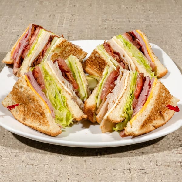 Four club sandwich halves, with ham, cheese, bacon, lettuce, and tomato, on a white plate.