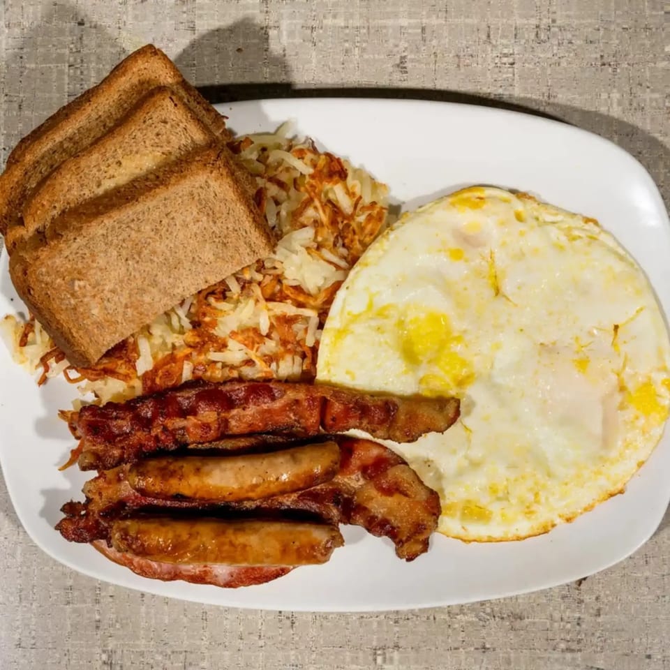 A full breakfast plate with fried eggs, hash browns, bacon, sausages, and toast.